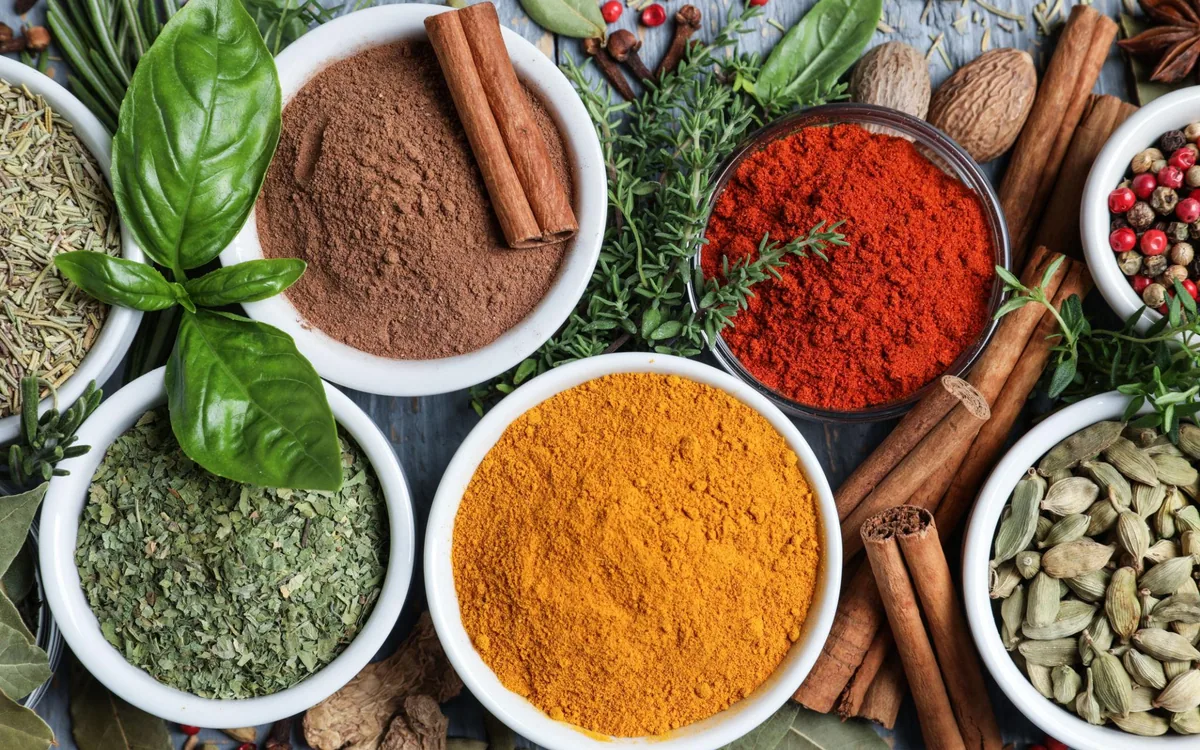 Ground chilli, turmeric, cinnamon and herb powders in white bowls with whole spices around them