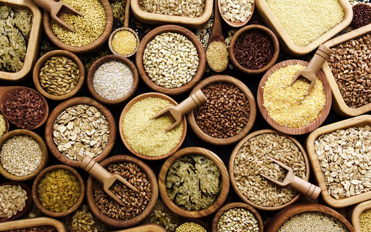 Rice, wheat, oats and other whole cereal grains in wooden bowls with scoops, seen from above