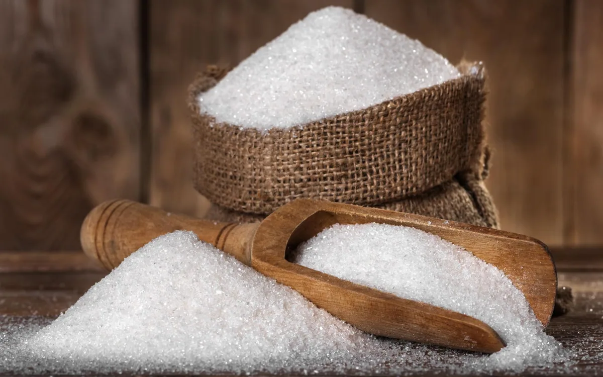 White granulated sugar spilling from a hessian sack with a wooden scoop