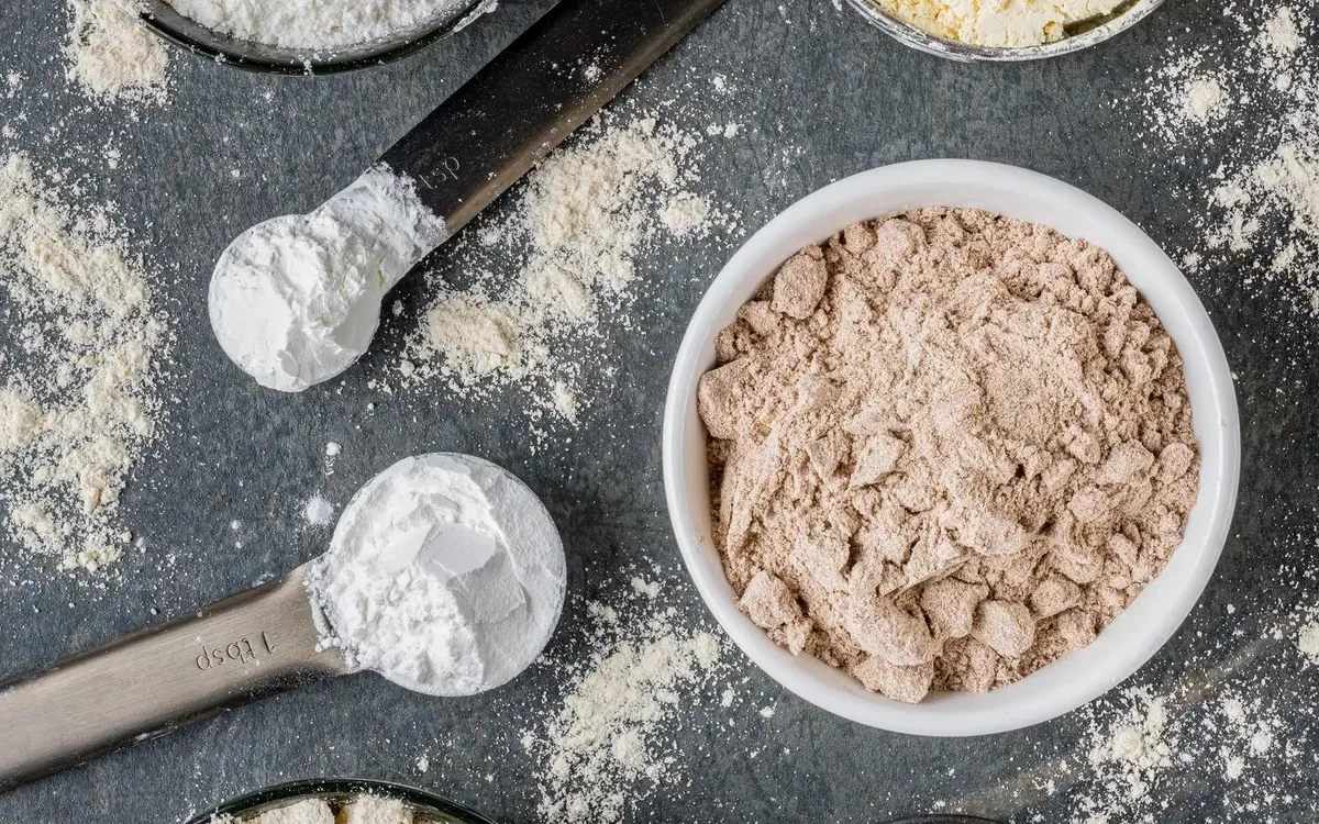 Whey and plant protein powders in bowls with measuring scoops on a dark surface