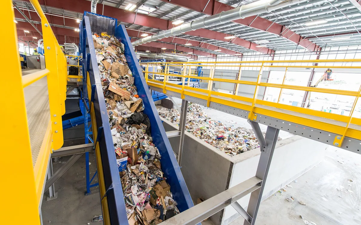 Baled cardboard and paper packaging moving up a conveyor inside a recovery facility